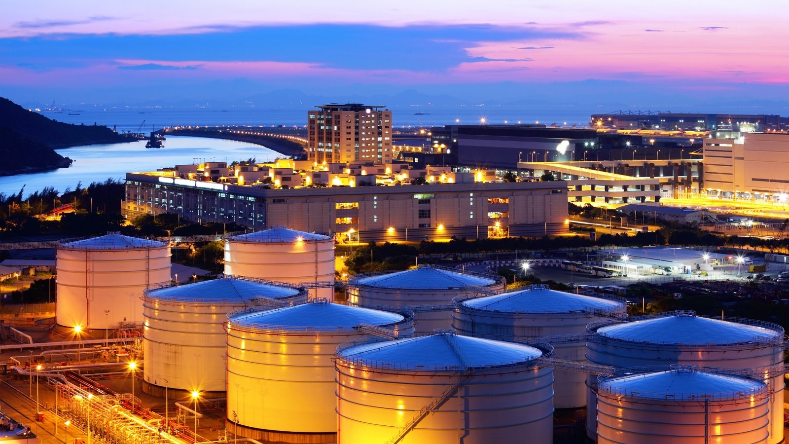 Crude storage at twilight: tank farms like these, commercial rather than sovereign, absorbed the Hormuz shock