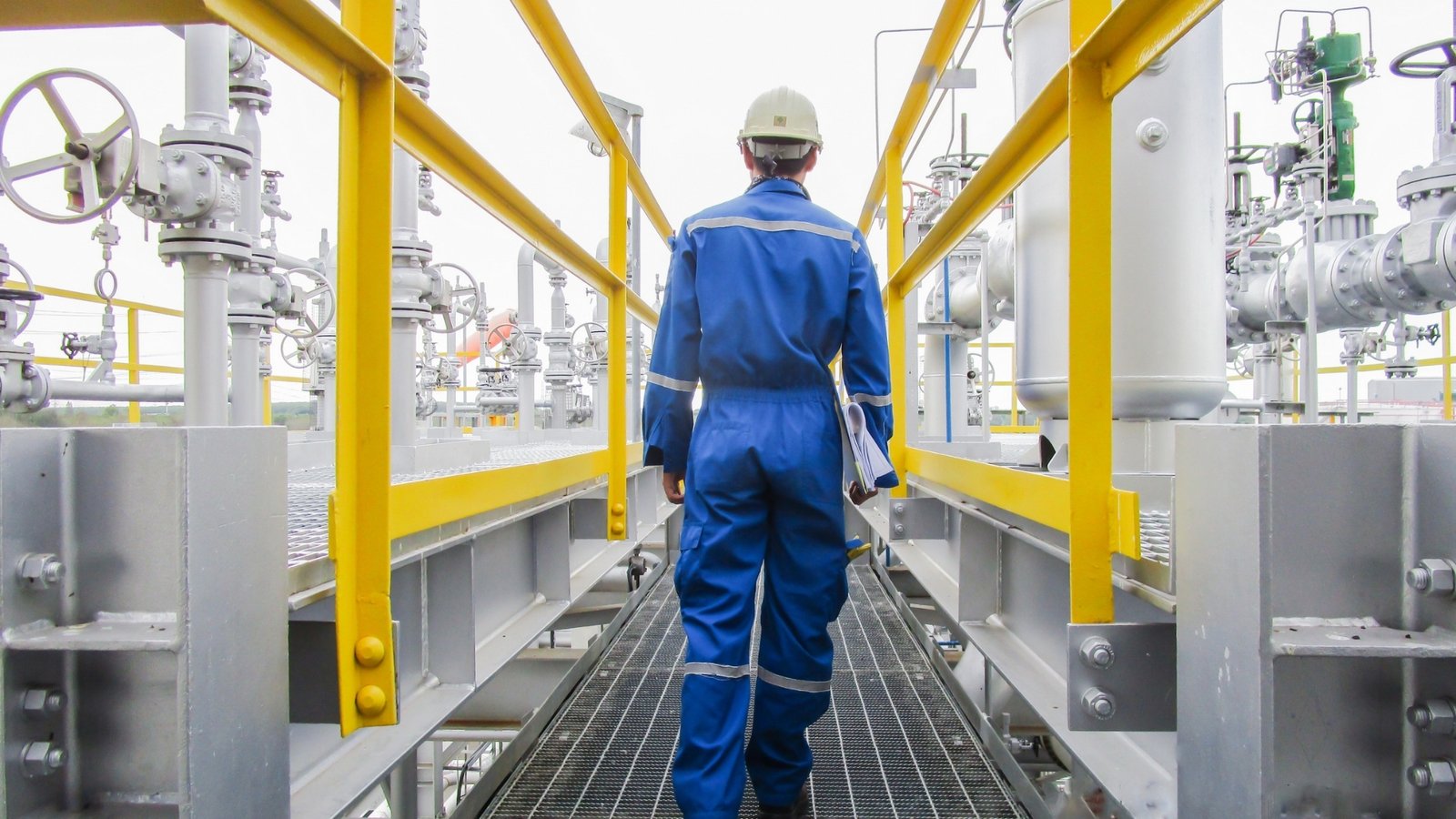 Engineer walking a gantry walkway through gas processing pipework