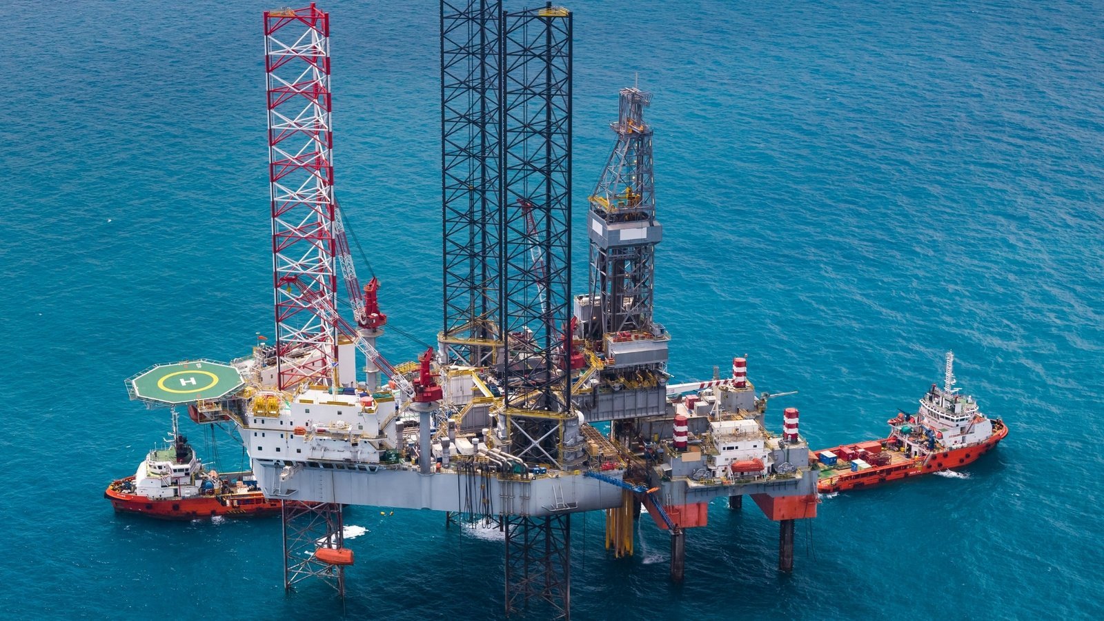 A jack up drilling rig and its support vessels offshore, the physical core of the oilfield services business SLB is now wrapping in digital and AI led revenue.