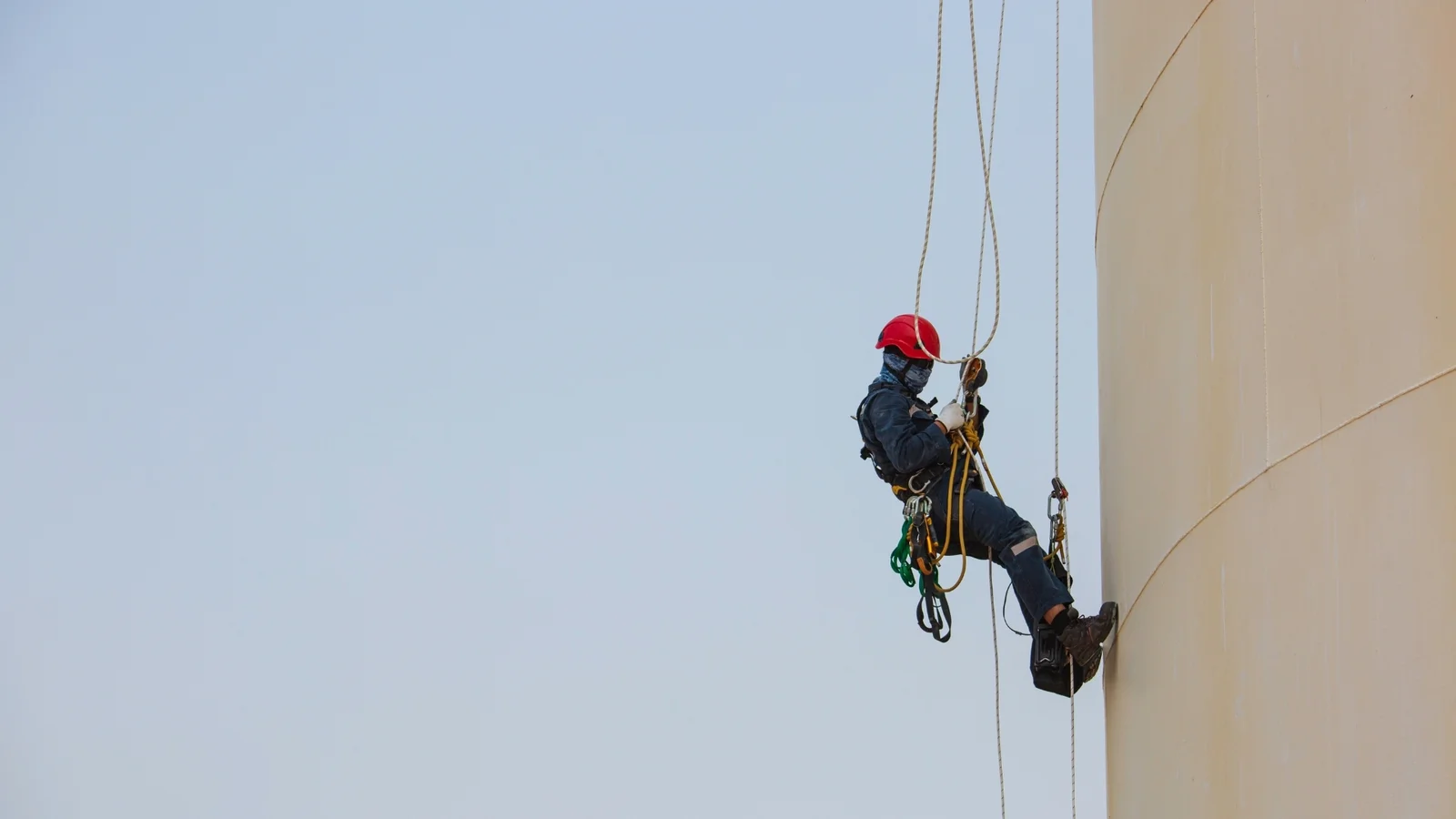 A rope access technician working alone on a storage tank. Positioning is engineered precision: a single, defensible place to stand.