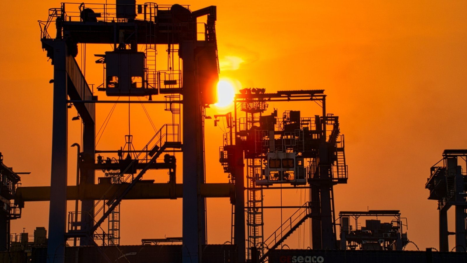 Refinery process structures silhouetted against an orange sunset sky