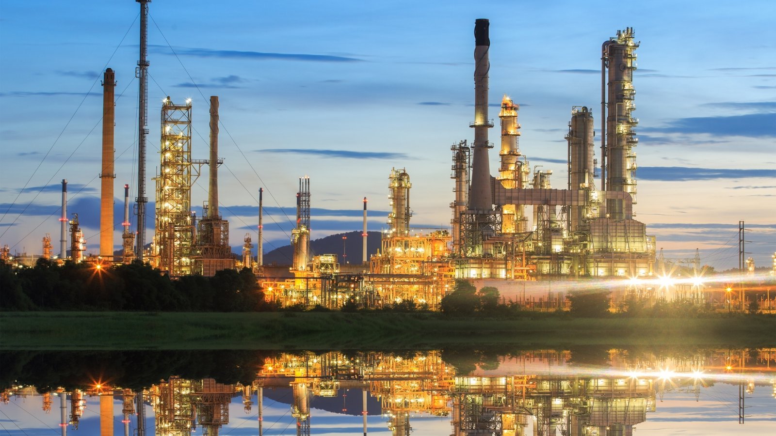 An integrated refining and petrochemical complex at first light, reflected in still water. Shell's 2030 targets remain intact while its capital increasingly concentrates in gas, liquids and trading-linked low-carbon businesses.