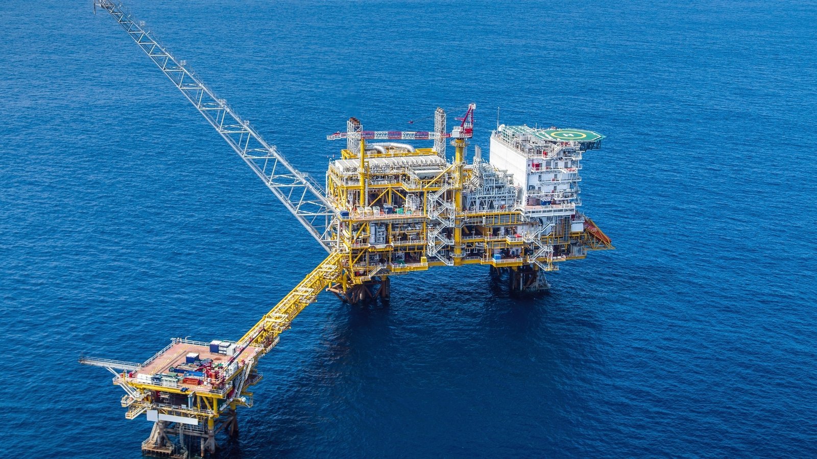 An offshore gas production platform linked by bridge to a wellhead structure. Santos moved Barossa and Pikka from construction into ramp during 2026, shifting the company from a build phase to a run phase.