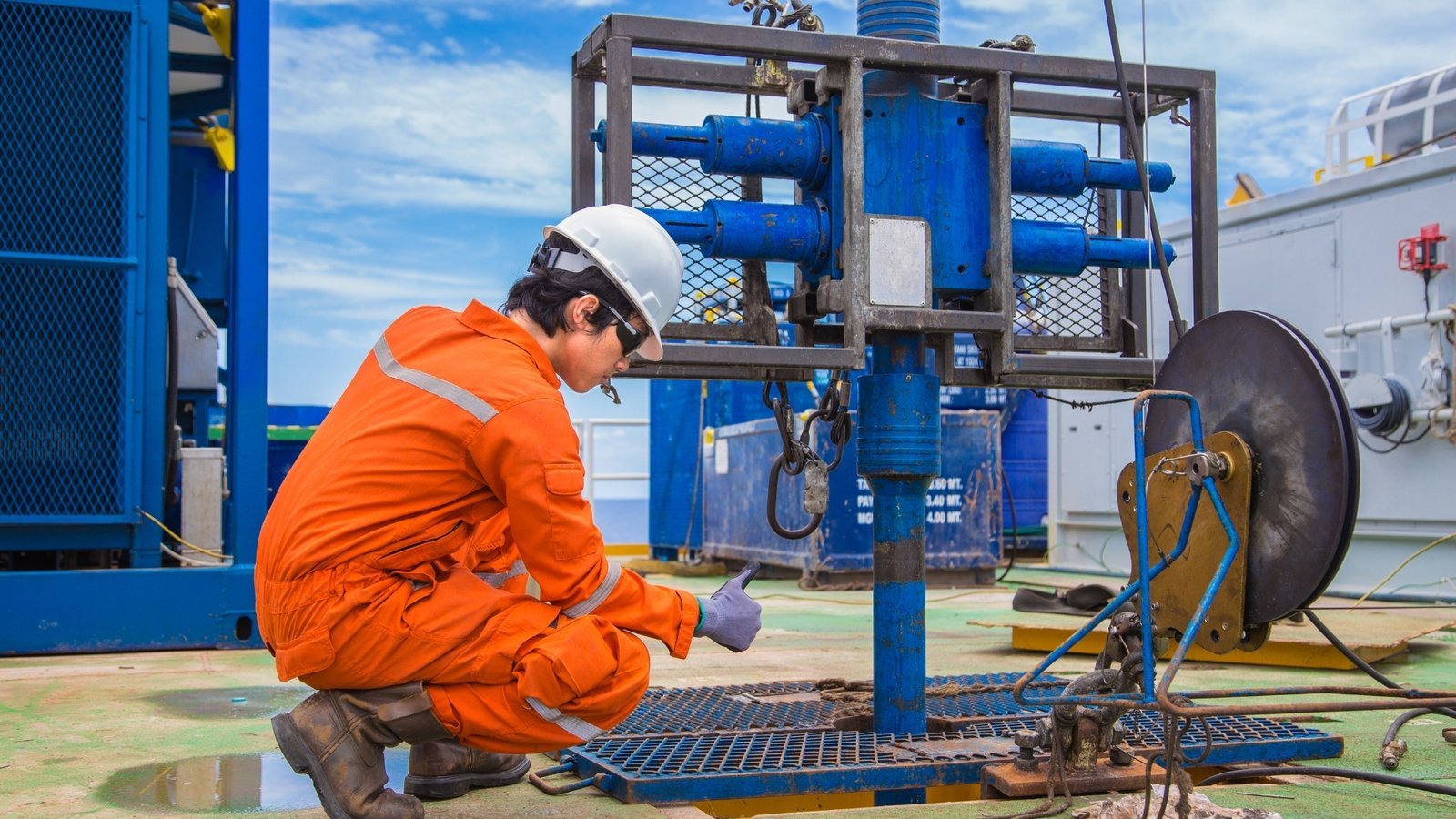 A technician in orange coveralls servicing instrumentation on a blue equipment skid