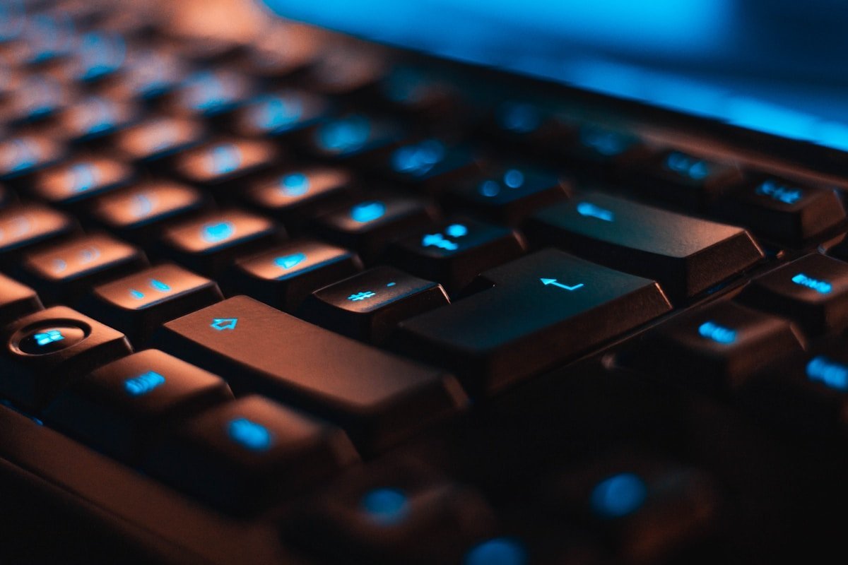 Close up of a backlit black computer keyboard with blue illuminated key symbols in a darkened room