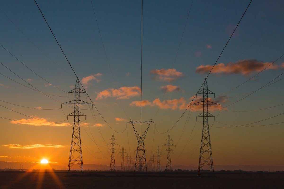 High voltage transmission towers at sunrise. The lines are built. The transformers and switchgear that connect new load to them are the part with a four year queue.