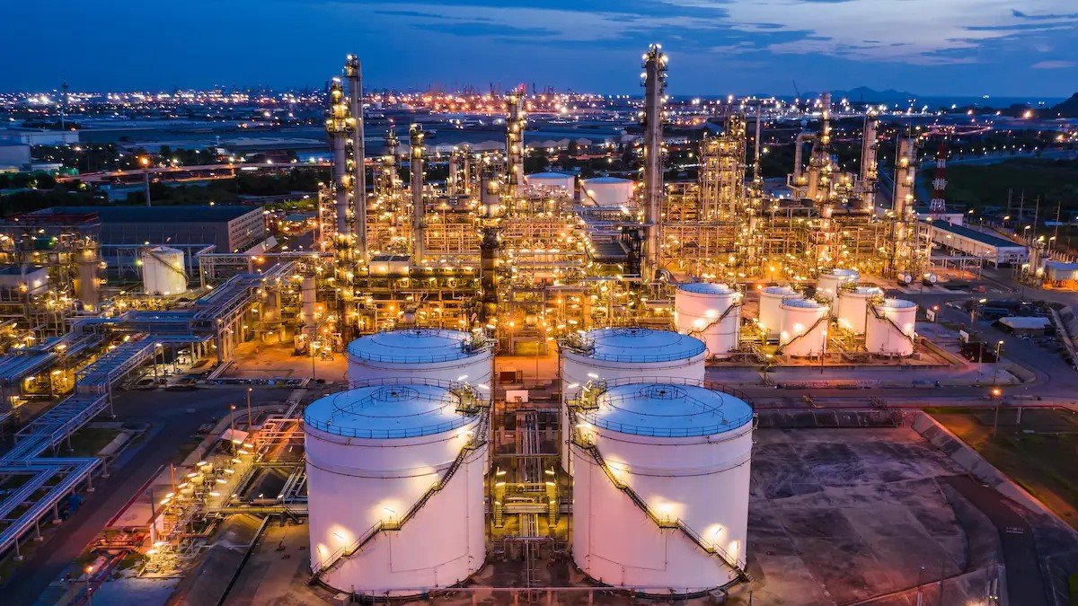 An LNG export terminal photographed from the air at dusk, rows of cylindrical storage tanks in the foreground and a jetty beyond