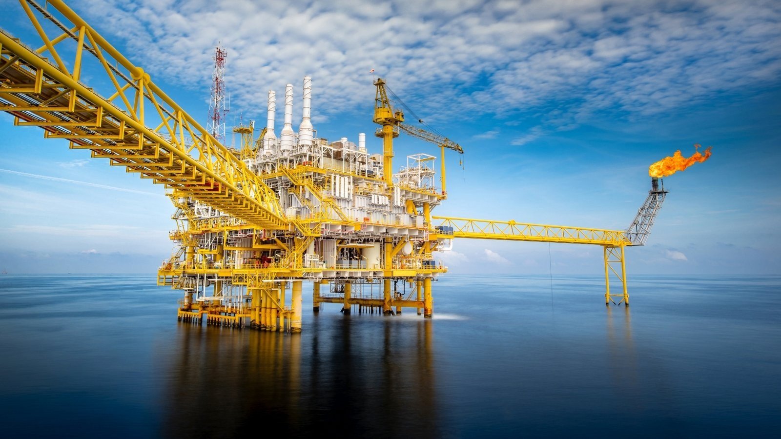 A bright yellow offshore gas production platform with a connecting bridge, photographed under clear skies above calm sea